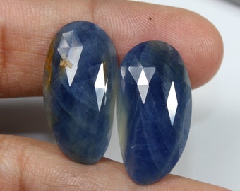 May include: Two blue sapphire gemstones with a faceted cut. The gemstones are oval shaped and have a light blue color with a hint of yellow.
