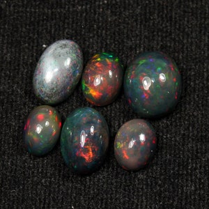May include: A collection of six oval-shaped opals. The opals display a variety of colors, including black, green, red, and orange, with iridescent flashes. The opals are set against a dark gray background.