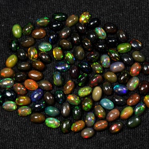 May include: A collection of oval-shaped black opal gemstones. The opals display a variety of colors, including green, blue, red, and yellow, with flashes of iridescence. The gemstones are scattered on a dark, textured surface.