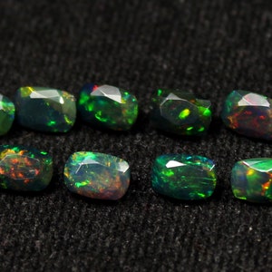 May include: Eight faceted black opal gemstones with vibrant flashes of green, orange, and red. The opals are displayed on a dark, textured surface, showcasing their unique color play and cut.