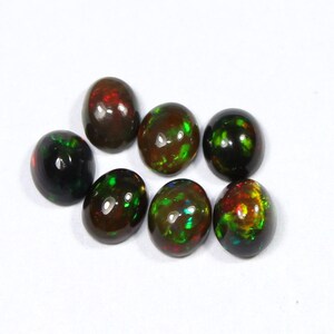 May include: Seven oval-shaped black opal gemstones with vibrant flashes of red, green, and yellow. The opals are polished and have a glossy finish, set against a white background. These gemstones are ideal for jewelry making.