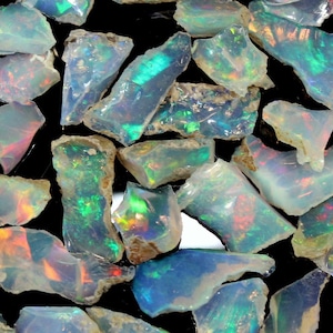 May include: A collection of rough, iridescent opal stones in various shapes and sizes. The opals are a mix of white, blue, green, and orange.