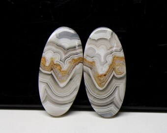 May include: Two oval-shaped agate cabochons with a white, gray, and brown banded pattern. The cabochons are smooth and polished.