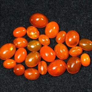 May include: A collection of orange oval-shaped gemstones, likely opals, displayed on a black surface.