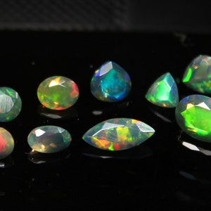 May include: A collection of nine opals in various shapes, including oval, pear, and round cuts. The opals display a vibrant play-of-color with flashes of green, blue, and red against a dark background. The gemstones are arranged to showcase their unique facets.