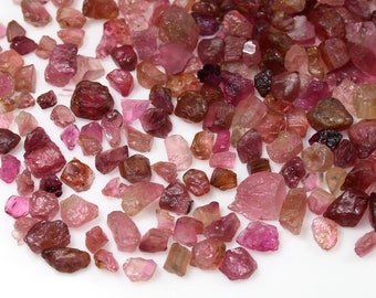 May include: A collection of pink and red rough gemstones. The gemstones are various shapes and sizes.
