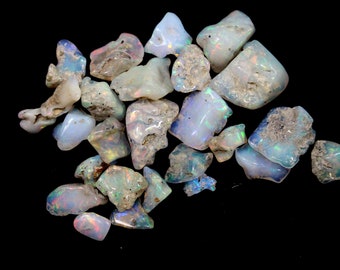 May include: A collection of rough, iridescent opal stones in various shapes and sizes. The stones are a mix of white, blue, and green hues with a rainbow sheen.