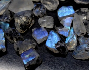 May include: A collection of iridescent moonstone chips in various shapes and sizes. The stones have a milky white base with blue and green iridescent flashes.