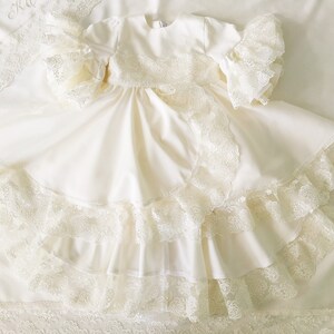 May include: A white lace christening gown with a ruffled skirt and long sleeves. The gown is made of a soft, delicate fabric and is perfect for a special occasion.