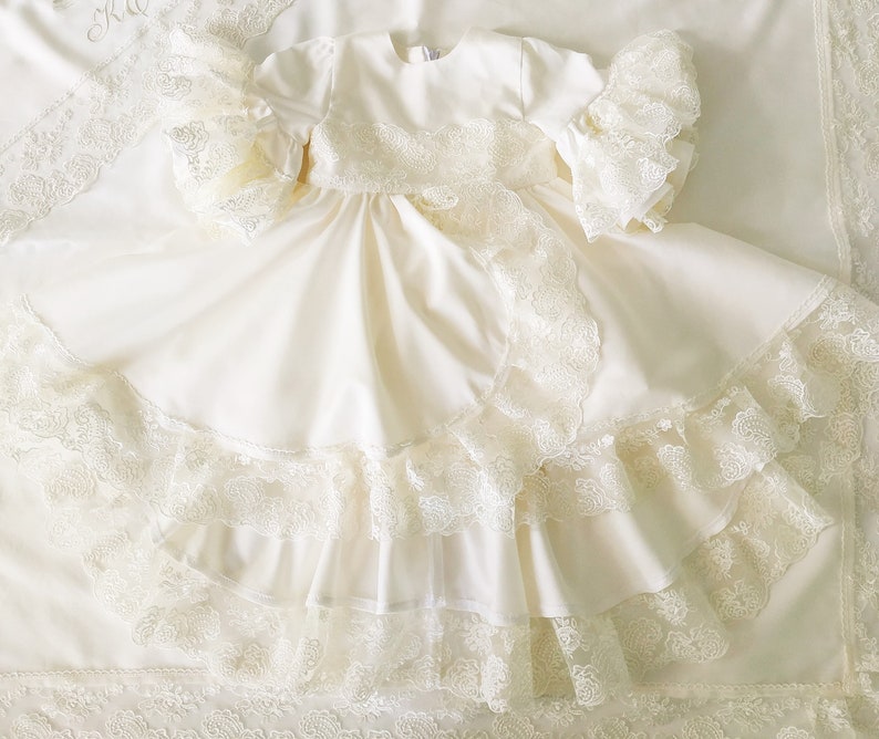May include: A white lace christening gown with a ruffled skirt and long sleeves. The gown is made of a soft, delicate fabric and is perfect for a special occasion.