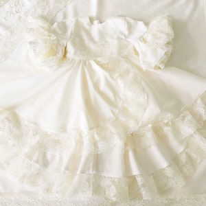 May include: A white, lace-trimmed dress with a ruffled skirt. The dress is made of a soft, flowing fabric and has a simple, elegant design.