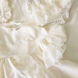 May include: A white satin dress with lace trim and ruffled sleeves. The dress has a simple, elegant design and is perfect for a special occasion.