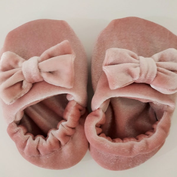 May include: A pair of pink velvet slippers with a bow on the top. The slippers are soft and comfortable.