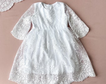 Puede incluir: Vestido blanco de encaje con mangas largas y dobladillo festoneado. El vestido está hecho de encaje delicado y tiene un diseño simple y elegante.