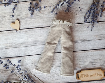 May include: A pair of beige corduroy trousers with a brown leather belt. The trousers have a wide leg and are made with a soft, comfortable fabric. The trousers are laid out on a wooden surface with dried lavender sprigs.