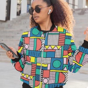 May include: A colorful geometric patterned bomber jacket with a zipper closure. The jacket has a mix of red, blue, green, yellow, pink, and black geometric shapes.