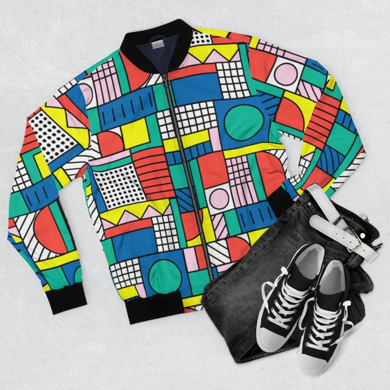 May include: A colorful geometric patterned bomber jacket with a black zipper and ribbed cuffs. The jacket is laid out on a white surface with black jeans and black sneakers.