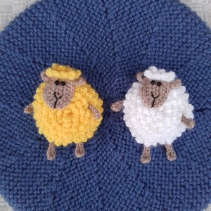 May include: Two knitted sheep on a blue knitted background. One sheep is yellow and the other is white.