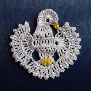 Könnte beinhalten: Weiße gehäkelte Taube mit gelben Akzenten. Die Taube ist ein Symbol des Friedens und wird oft in der religiösen Kunst verwendet.
