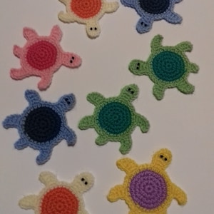 May include: Eight crocheted turtle coasters in various colors, including pink, blue, green, yellow, and orange. Each coaster features a circular design in the center.