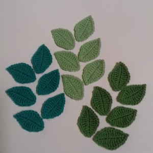 Puede incluir: Una colección de hojas de ganchillo verdes y azul verdoso. Las hojas están dispuestas en forma de semicírculo.