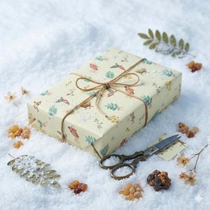 May include: A rectangular gift box wrapped in cream-colored paper featuring a repeating pattern of small botanical illustrations, including green leaves, brown acorns, and flowers, tied with thin brown twine and accompanied by metal scissors.