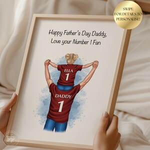 Puede incluir: Una impresi&oacute;n enmarcada con un marco de madera clara. La obra de arte representa a una persona que lleva a un ni&ntilde;o sobre sus hombros, ambos con camisetas granates con el n&uacute;mero 1. El texto dice "Happy Father's Day Daddy, Love your Number 1 Fan."