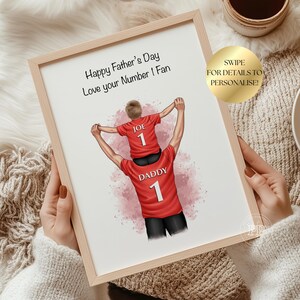 Puede incluir: Una impresi&oacute;n enmarcada con el texto "Happy Father's Day Love your Number 1 Fan". La ilustraci&oacute;n muestra a un padre y su hijo con camisetas rojas con el n&uacute;mero 1. El hijo est&aacute; sobre los hombros del padre.