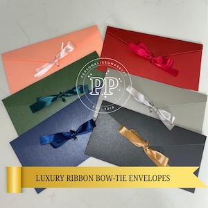 May include: A collection of luxury ribbon bow-tie envelopes in various colors, including coral, green, red, gray, navy, and black. Each envelope is adorned with a matching satin ribbon bow. The text "LUXURY RIBBON BOW-TIE ENVELOPES" is displayed.
