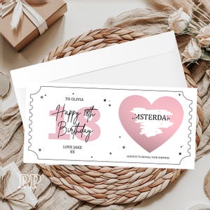 May include: A white birthday card with a pink heart and the text "Happy 18th Birthday." The card includes the text "To Olivia" and "Love Jake XX." The card is on a woven surface with a white envelope.