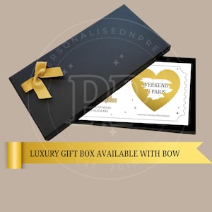May include: A black gift box with a gold bow, open to reveal a card. The card has a gold heart with the words "WEEKEND IN PARIS" and the text "SCRATCH TO REVEAL YOUR SURPRISE". The box also has the text "LUXURY GIFT BOX AVAILABLE WITH BOW".