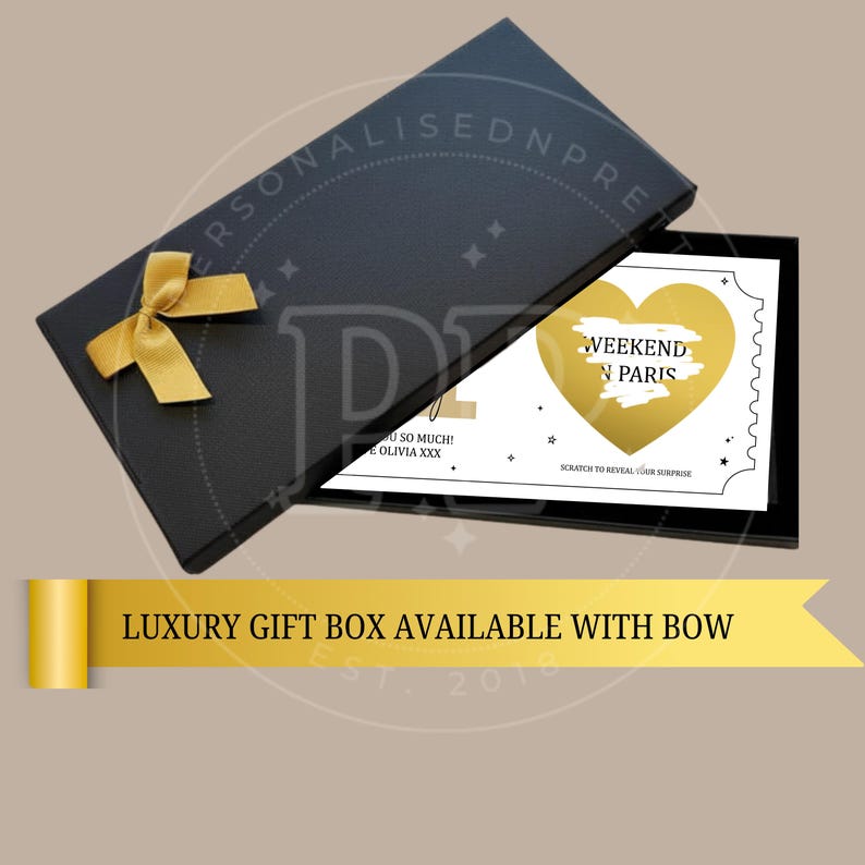 May include: A black gift box with a gold bow, open to reveal a card. The card has a gold heart with the words "WEEKEND IN PARIS" and the text "SCRATCH TO REVEAL YOUR SURPRISE". The box also has the text "LUXURY GIFT BOX AVAILABLE WITH BOW".