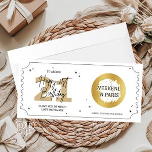 May include: A white birthday card with black and gold text, and a gold scratch-off circle. The card reads "Happy 21st Birthday" and "Weekend 'N Paris". The card is on a woven mat with a white envelope.