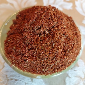 May include: A close-up of a small bowl filled with a blend of red, brown, and beige spices. The spices are finely ground and have a slightly grainy texture.