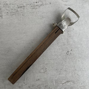 Pode incluir: Um abridor de garrafas de madeira e metal com uma pega de madeira castanho e um abridor de metal prateado.