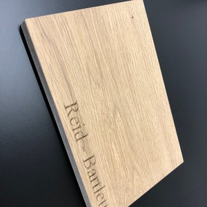 May include: A light brown wooden cutting board with the name "Reid - Bartley" engraved on the surface.