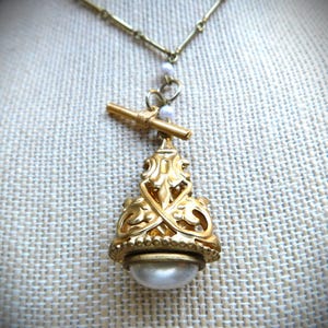 Puede incluir: Un collar de oro con un colgante decorativo que presenta una perla grande y un diseño filigrano intrincado.