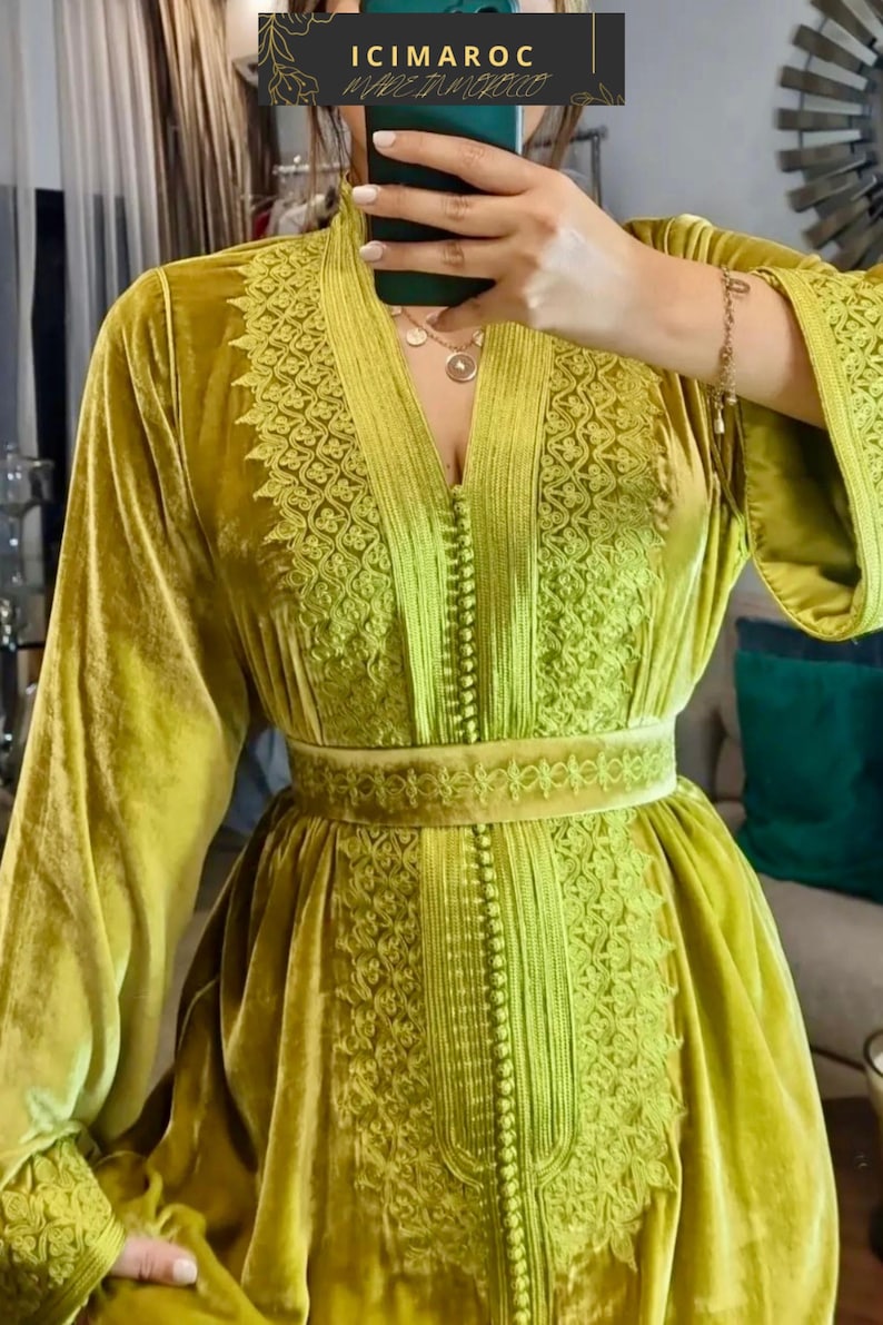 A woman in a chartreuse velvet caftan with a V-neck and embroidered details on the bodice, sleeves, and belt, taking a mirror selfie.