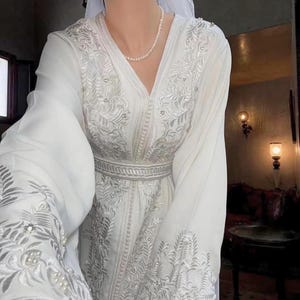 Model wearing white Moroccan caftan with white thread design, long sleeves, perfect for nikah ceremony.