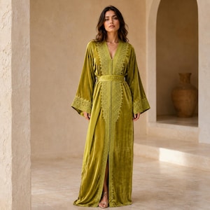 May include: A floor-length olive green velvet kaftan featuring long, wide sleeves and a deep V-neckline. The garment is adorned with intricate tonal embroidery along the center front placket, waist, and sleeve cuffs, finished with a central row of buttons.