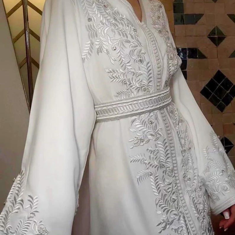 Close-up of embroidered sleeves and belt on white Moroccan caftan, handcrafted detail for Muslim bride.