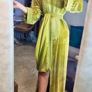 A woman in a chartreuse velvet caftan with a thigh-high slit, embroidered trim, and a matching belt, posing in front of a mirror.