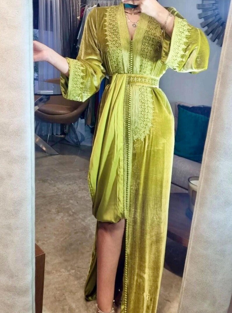 A woman in a chartreuse velvet caftan with a thigh-high slit, embroidered trim, and a matching belt, posing in front of a mirror.