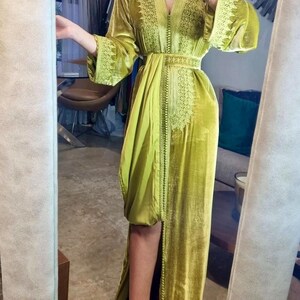 A woman in a chartreuse velvet caftan with a high slit and embroidered trim, posing in a mirror, showing the full length of the dress.