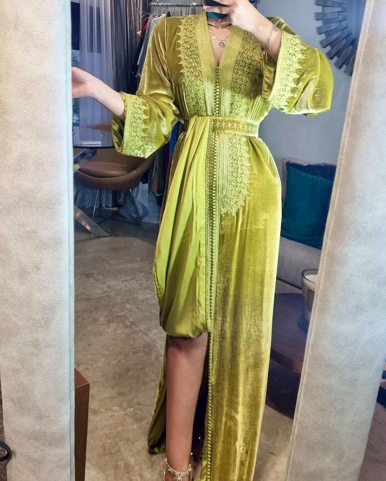 A woman in a chartreuse velvet caftan with a high slit and embroidered trim, posing in a mirror, showing the full length of the dress.