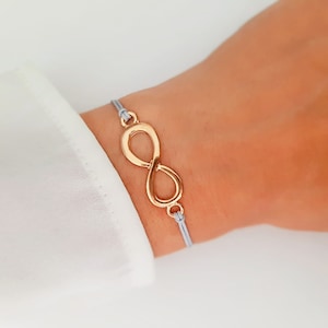 Puede incluir: Un brazalete de cordón gris con un dije de infinito de oro.