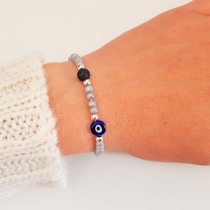 Puede incluir: Un brazalete de cuentas grises con un dije de ojo turco azul y una cuenta de lava negra.