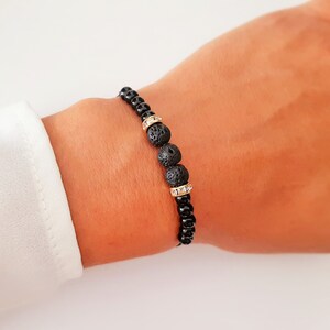 Op de afbeelding: Een zwarte kralen armband met drie grotere zwarte lavastenen versierd met goud en heldere strass.