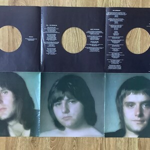 May include: A black and white vinyl record album cover with three men's portraits on the bottom half. The top half features three blank circles for the records and song lyrics.