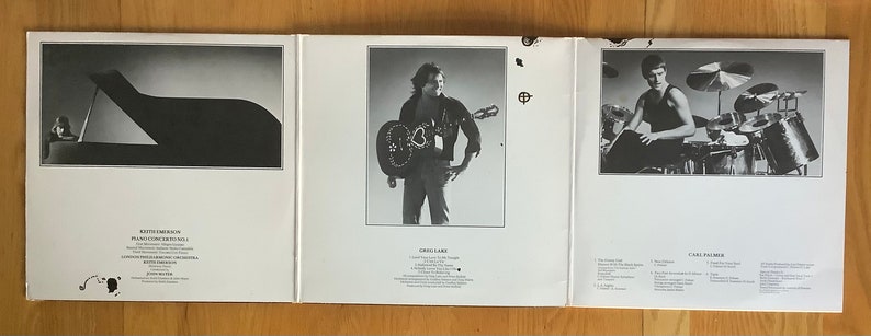 May include: A black and white photograph of a piano with a person sitting at the keys. The photo is on the left side of a record album cover. The right side of the cover features a black and white photograph of a man playing a guitar. The bottom of the cover has text listing the songs on the album.
